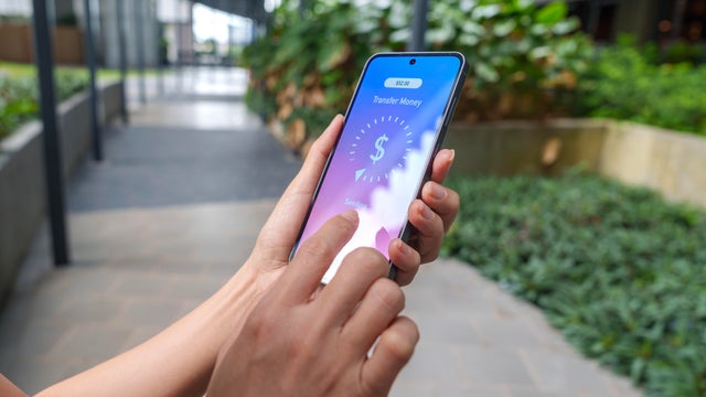 A person uses a smartphone app to transfer money while outdoors. 