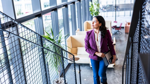 Confident businesswoman walking up modern office staircase and looking out window 
