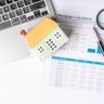 Calculating mortgage options and financial planning with a calculator, laptop, and house model at a workspace 