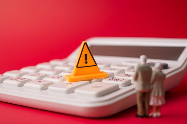 Senior couple looking at yellow warning sign on white calculator with red background. 