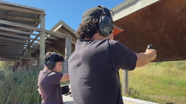 two people shooting guns at a firing range while wearing safety gear 