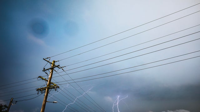 Storm with rainbow and dark dramatic sky, clouds over power lines and electricity poles 