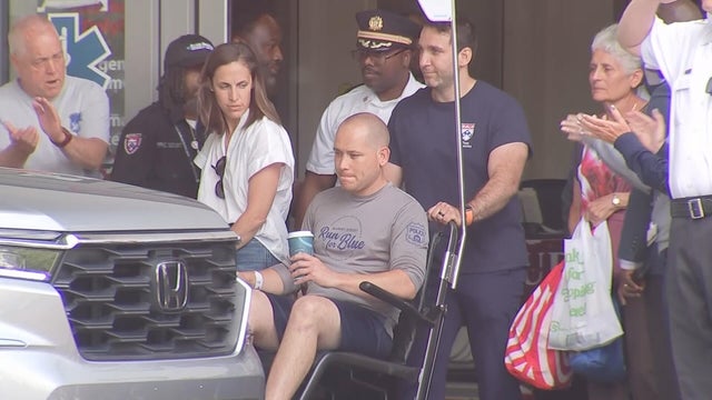 A police officer is wheeled out of the hospital as officers look on and cheer for him 