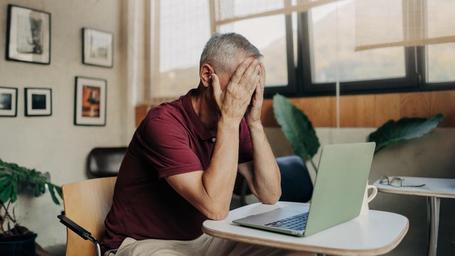Tired and upset mature man uses laptop 