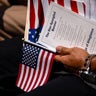 An attendee holds the U.S. flag and lyrics of the national anthem at a naturalization ceremony at George Washington's Mount Vernon in Mount Vernon, Virginia, on July 4, 2025. 