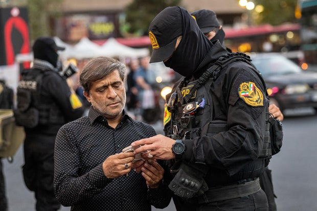 An Iranian policeman checks the cellphone of a man who had been taking pictures in the street on July 3, 2026, in Tehran, Iran, as the country began a week of funeral ceremonies for its former supreme leader, Ayatollah Ali Khamenei.