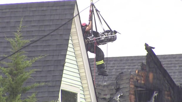 A firefighter being hoisted with ropes above a fire-damaged home 