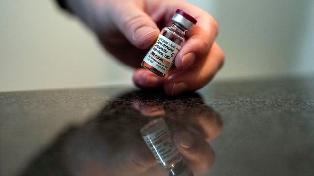 A person administers an injection in their own arm using a small syringe 
