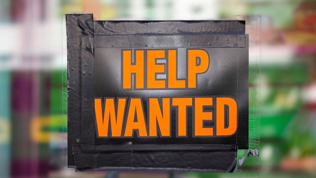 Bright orange "Help Wanted" sign taped to a window, symbolizing job opportunities, hiring, and employment recruitment 