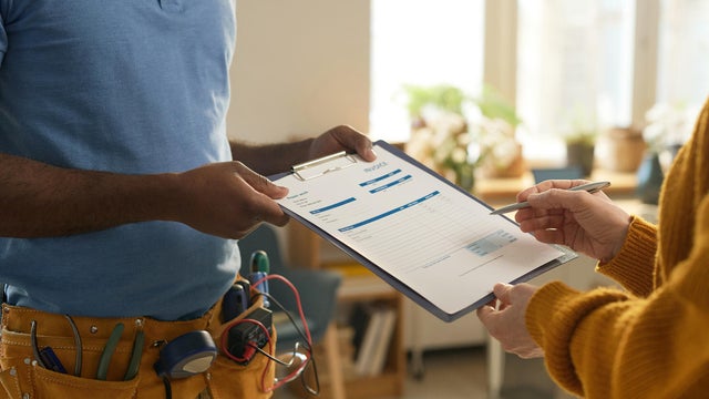 Man with Toolbelt Handing Clipboard to Client 