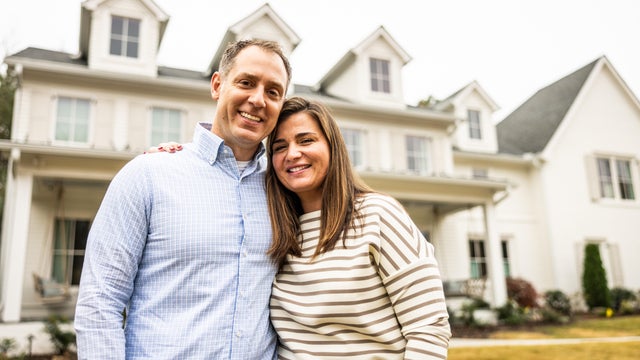 Portrait of married couple standing in front of suburban home 