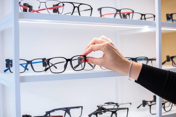 Hand of unrecognizable woman reaches out to touch pair of eyeglasses lying on display