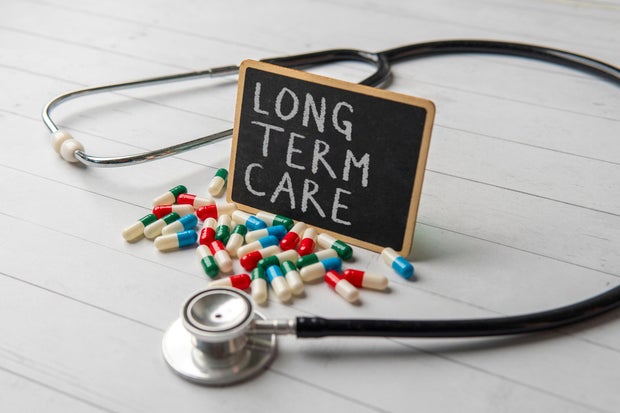 A chalkboard with the words LONG TERM CARE surrounded by scattered pills and a stethoscope. 