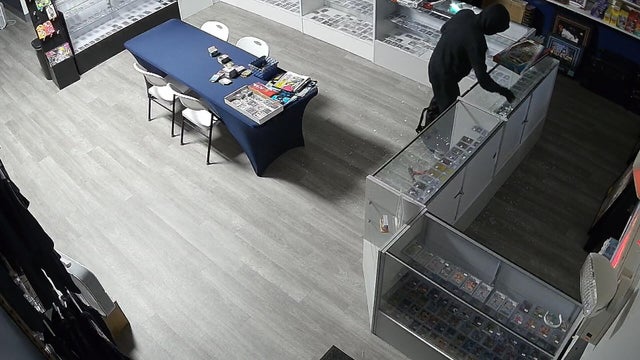 Still image from a surveillance video of a thief reaching into a display case 