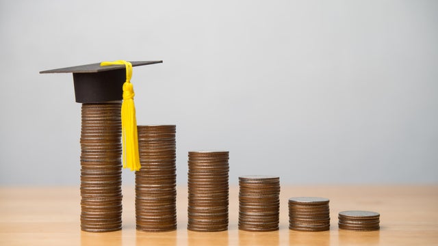 Mortarboard or square academic cap and reduce stack coins chart on wooden table with white wall background. 