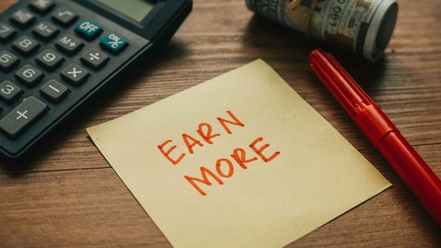 Selective focus of calculator,money pen and paper written with Earn More. 