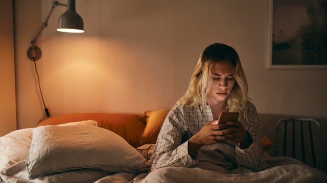 Transgender person using mobile phone sitting on bed at home 