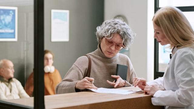 Woman Signing Medical Forms at Clinic Reception Desk 