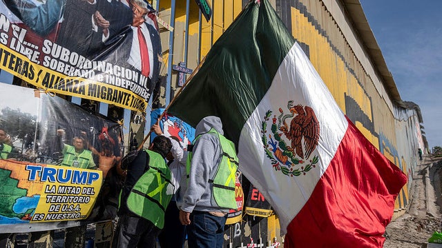Demonstrators hang a Mexican flag alongside protest banners and crosses on the U.S. border wall in Playas de Tijuana, Baja California state, Mexico on Dec. 18, 2025. 