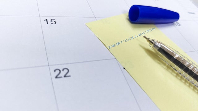 A pen and sticky note labeled "Debt Collection" rest on a calendar, highlighting an upcoming payment deadline. 