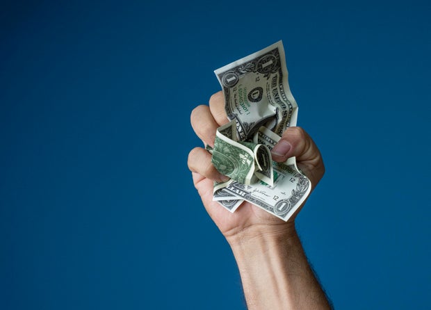 Hand Clenching Crumpled US Dollar Bills Against Blue Background 