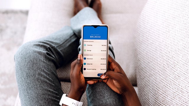Overhead view of young Black woman managing online banking with smartphone sitting on the sofa at home. 