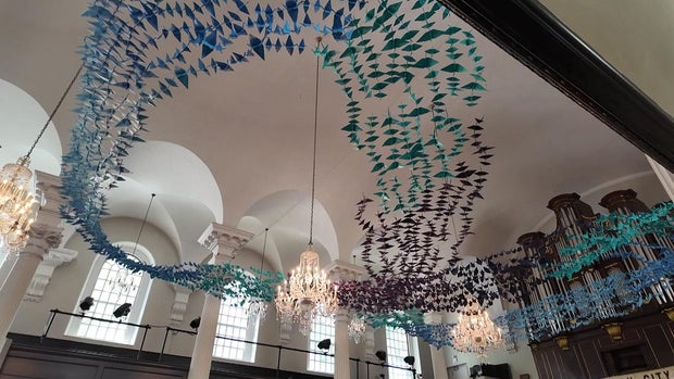 Hundreds of blue paper cranes hung in the shape of an infinity symbol from the ceiling of a church 