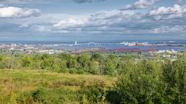 Expansive scenic view of a city and industrial port along a large body of water under a cloudy sky, seen from a high vantage point,Duluth,United States,USA 
