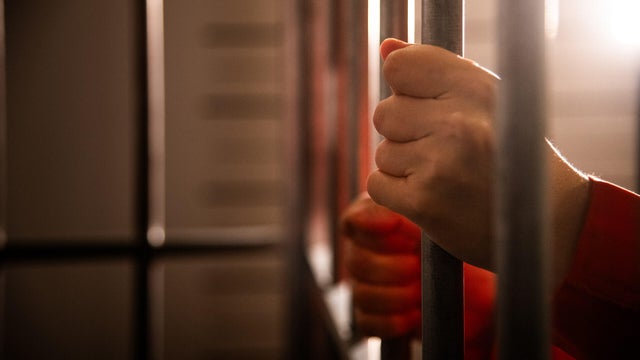 Prisoner's hands holding prison bars 