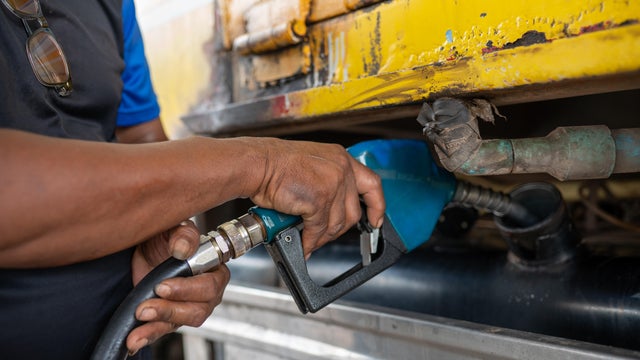 A man is filling up a yellow truck with gas 