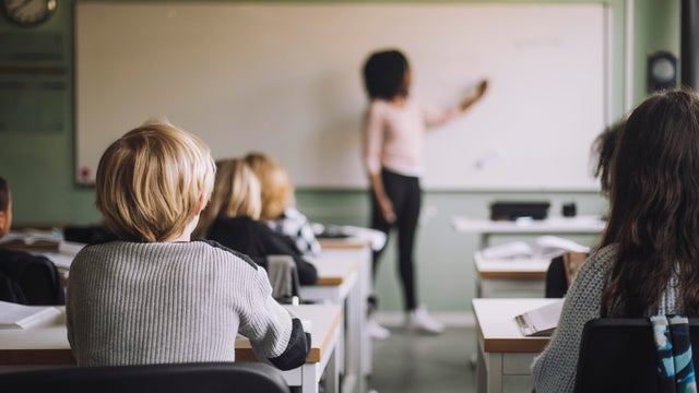 Rear view of students sitting at desk while teacher teaching in classroom 