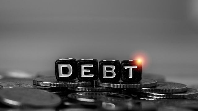Debt concept with letter blocks on stacked coins in monochrome tone. Financial crisis, loan repayment, credit risk, bankruptcy, economic downturn and personal finance problem background. 