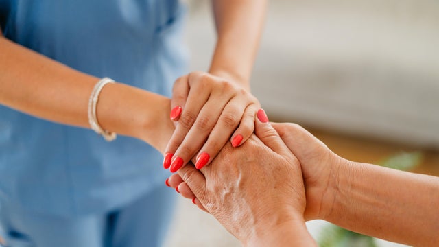 Home Care Nurse Holding Hands With A Mature Woman At Her Home 