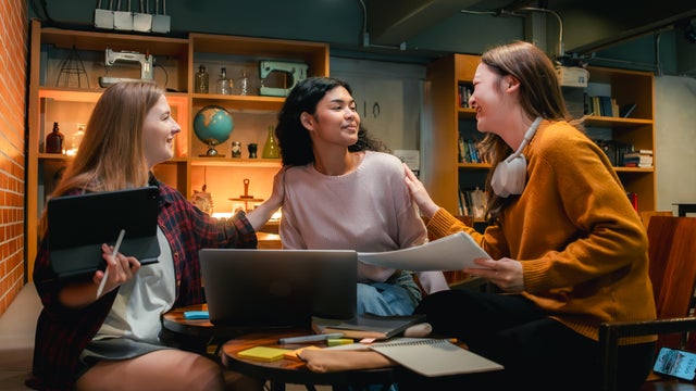 Supportive friends helping their roommate study for an exam at night in the dormitory 