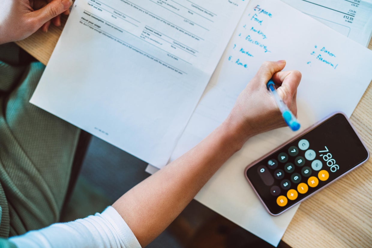 Overhead view of young Asian women managing home finance using smartphone. She is working with household utility bill and  calculating expenses at home. 