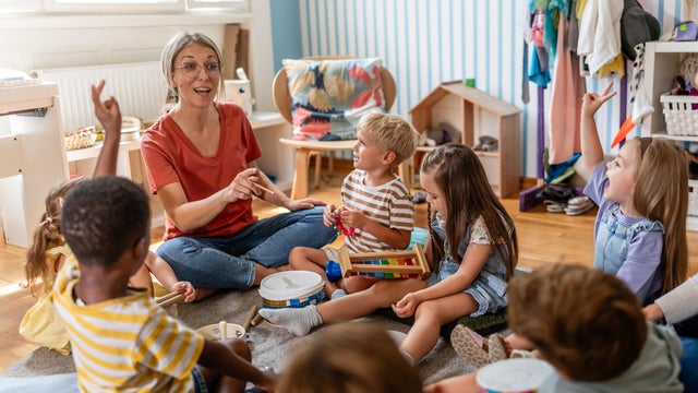 Teacher engaging a diverse group of preschool children in a fun indoor activity, sitting together in a circle and developing social and learning skills in a cozy kindergarten classroom 
