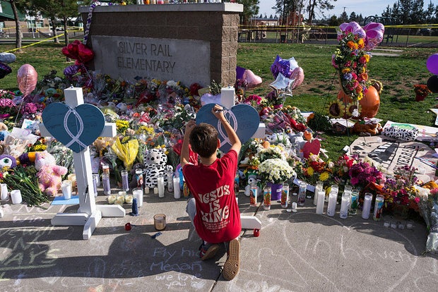 A child writes a message on a cross at a memorial at Silver Rail Elementary School in Bend, Oregon Saturday morning.