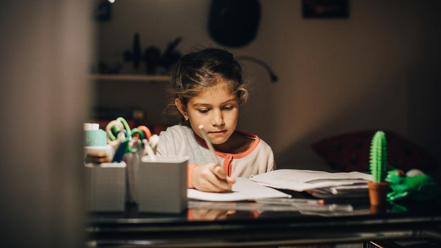 Girl writing homework on desk while sitting against wall at home 