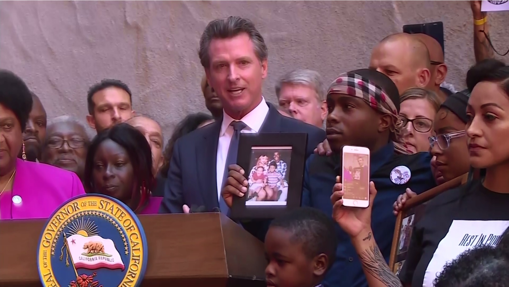 Surrounded by relatives of people killed in police shootings, Gov. Gavin Newsom signed AB392 at a ceremony in Sacramento on August 19, 2019. (CBS)